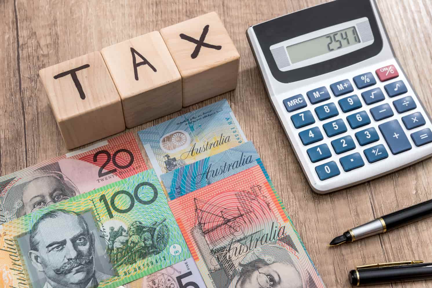 Australian dollars next to a pocket calculator and three wooden cubes with the word "tax" written on them
