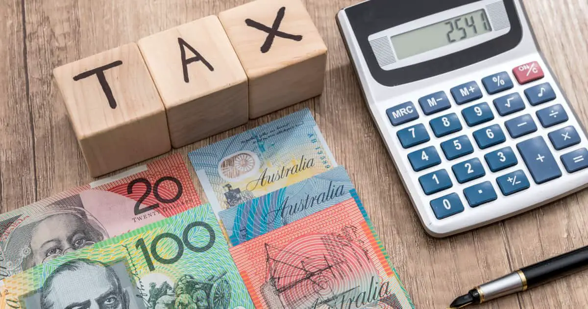 Australian dollars next to a pocket calculator and three wooden cubes with the word "tax" written on them