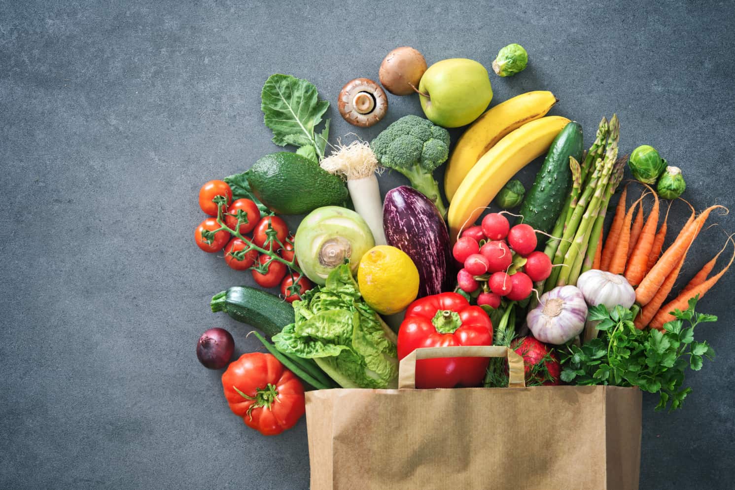 A paper shopping bag full of fresh vegetables and fruits
