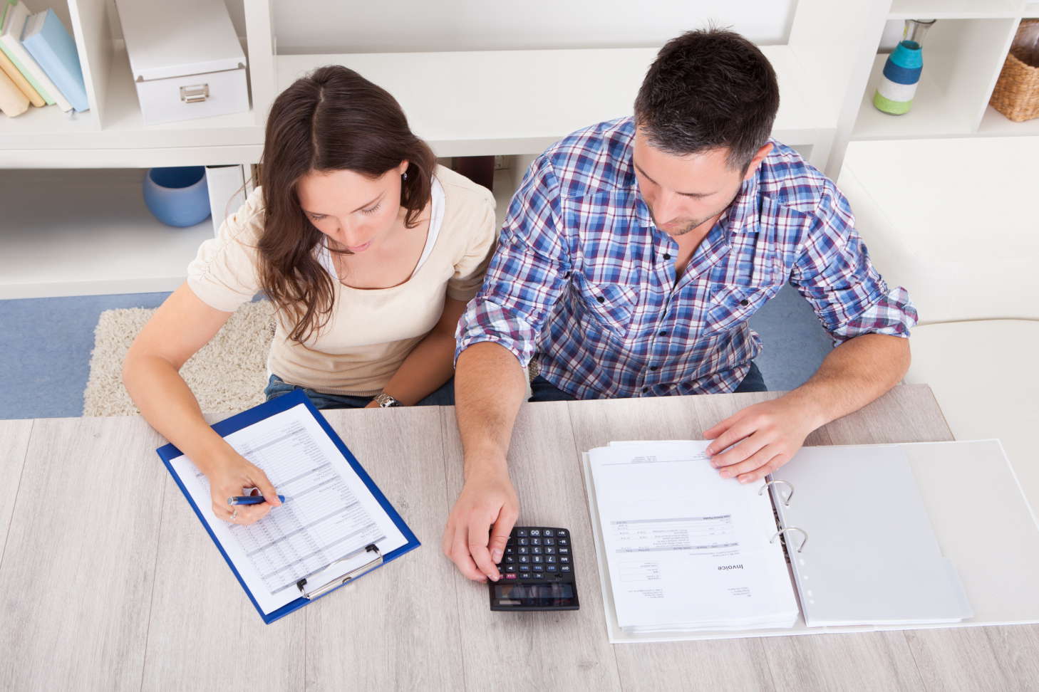 A young couple checking their tax forms using a pocket calculator