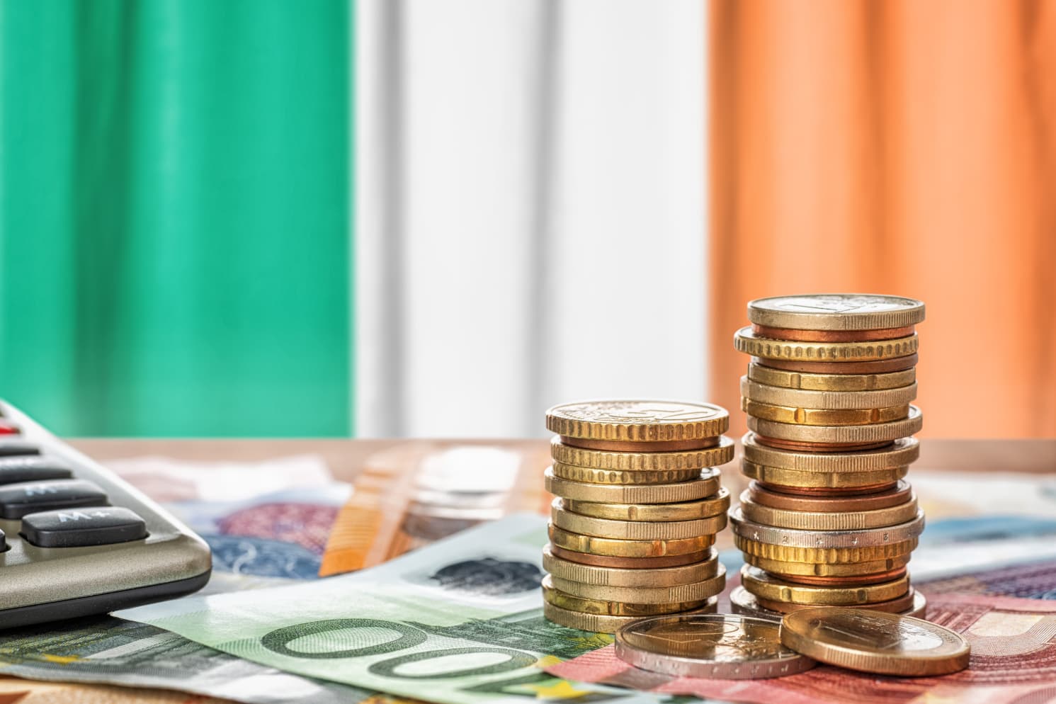 Euro banknotes, coins and a calculator in front of the national flag of Ireland