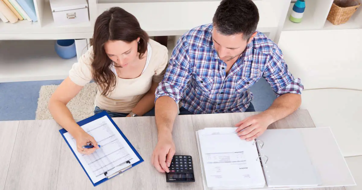 A young couple checking their tax forms using a pocket calculator
