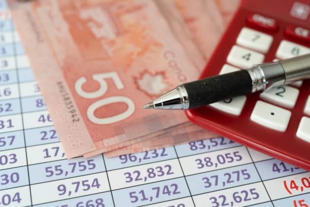 Canadian dollar banknotes spread across an accounting worksheet next to a red pocket calculator